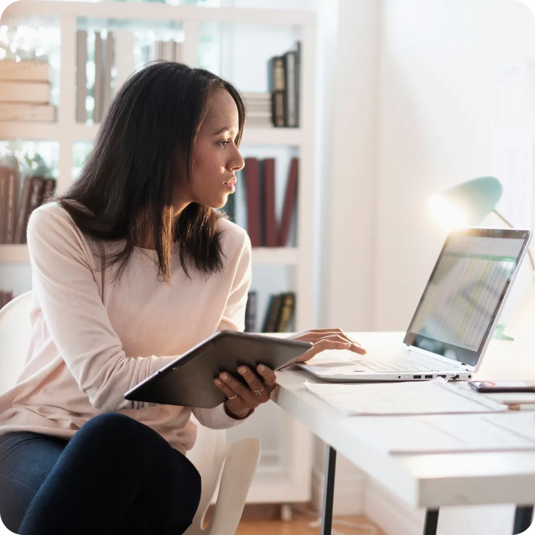 User holding a tablet and looking at their laptop to start their 30 day free trial with Duo.