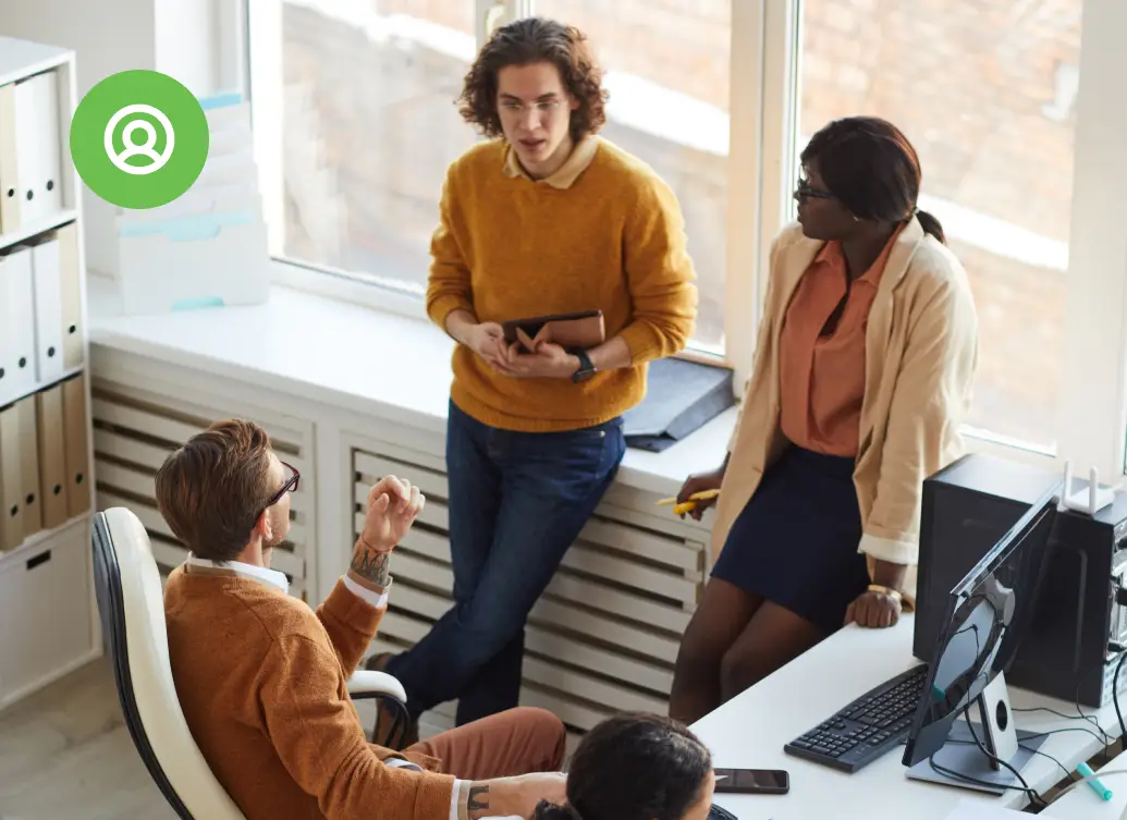 Four colleagues discuss a project around a desk with laptops and documents in a modern office
