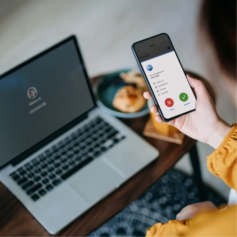 A person is holding a smartphone displaying a two-factor authentication screen with options to approve or deny a login attempt.