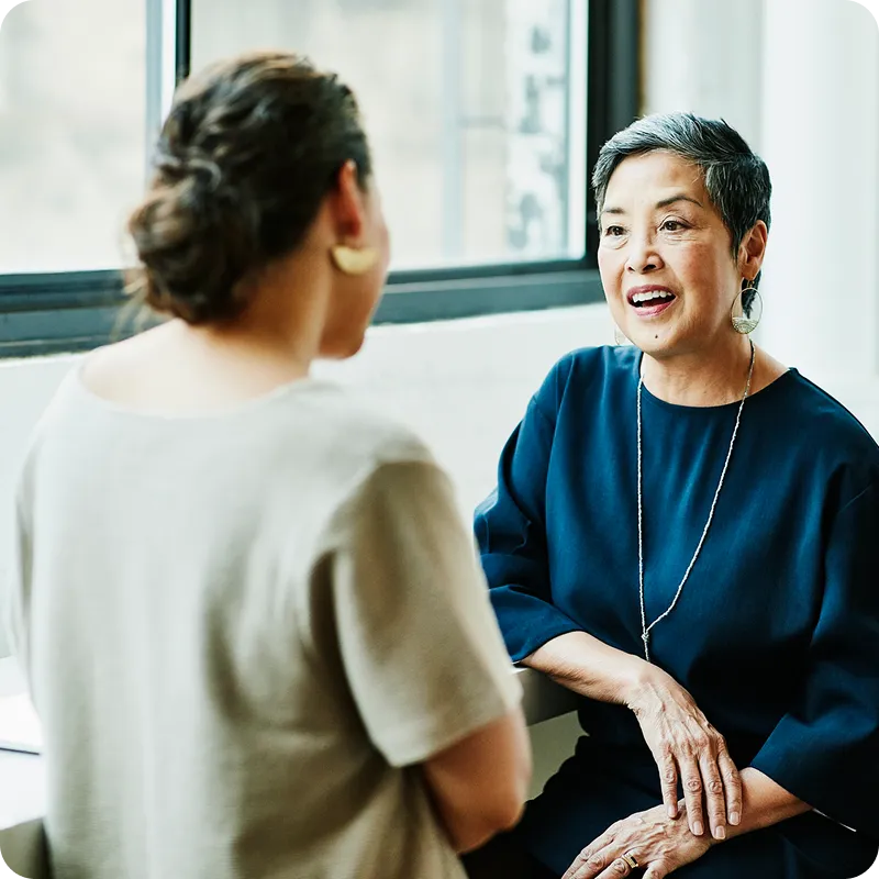 Women in an office talking to each other. Left of photo are button icons for mobile phone functions.